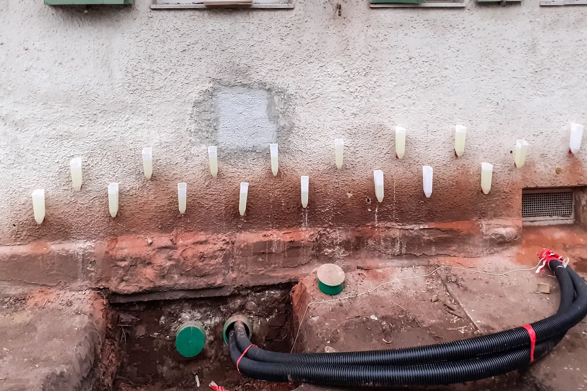 Damp specialist checking a damp patch at the base of an interior wall with a moisture meter
