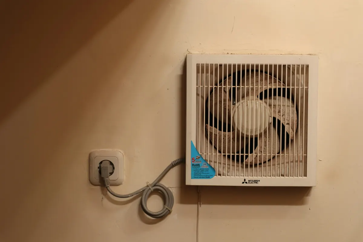 White humidistat extractor fan fitted high on a tiled bathroom wall